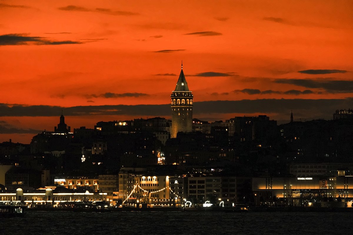 Turuncu gün batımı gökyüzünün önünde ışıklandırılmış Galata Kulesi ve Karaköy sahili