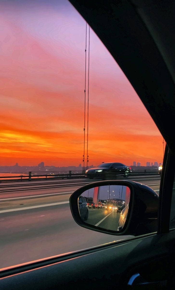 Araba camından turuncu ve mor gün batımı, yan aynada köprü trafiği